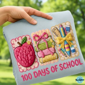 Pu&ograve; includere: Una felpa azzurra con disegni ricamati per la celebrazione dei "100 giorni di scuola". Il design include una mela rosa, rocchetti di filo e materiale scolastico. Il testo "100 DAYS OF SCHOOL" &egrave; ricamato in rosa.