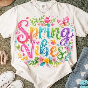 May include: White t-shirt with the words "Spring Vibes" in colorful, whimsical lettering. The design includes flowers, butterflies, and leaves, creating a cheerful, spring-themed graphic.