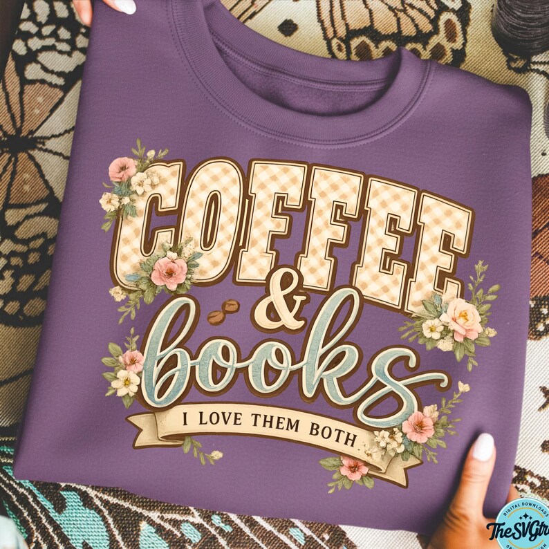 Op de afbeelding: Een paarse sweatshirt met de tekst "COFFEE & books" in een decoratief lettertype, versierd met bloemmotieven. De tekst "I LOVE THEM BOTH" staat eronder. De sweatshirt wordt vastgehouden door de handen van een persoon.