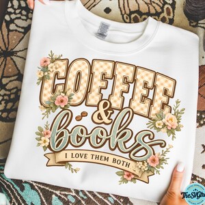 Op de afbeelding: Witte sweatshirt met de tekst "COFFEE & books" in een decoratief lettertype, met bloemaccenten. De tekst "I LOVE THEM BOTH" staat eronder. Het ontwerp bevat koffiebonen en bloemen in roze, beige en groene tinten.