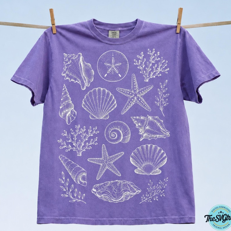 Puede incluir: Una camiseta morada con ilustraciones blancas de conchas marinas, incluyendo estrellas de mar, caracolas y coral. La camiseta est&aacute; colgada en un tendedero sobre un fondo azul claro. El dise&ntilde;o es una descarga digital de The SVG Girl.