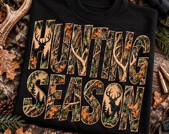 May include: A black crewneck sweatshirt featuring the text HUNTING SEASON in large block letters. The letters are filled with a camouflage pattern of tree bark, leaves, and pine needles, with silhouettes of deer and pine trees integrated.