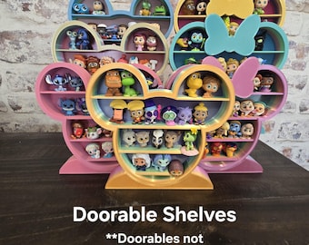 May include: A collection of colorful, Mickey Mouse-shaped shelves in pink, blue, and yellow. Each shelf has multiple levels to display small figurines. The text "Doorables Shelves" is at the bottom of the image.