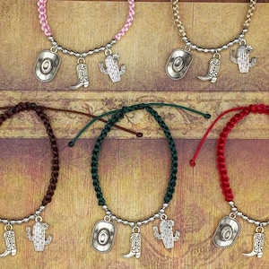 May include: Five different colored friendship bracelets with silver charms. The charms include a cowboy hat, a cactus, and a cowboy boot. The bracelets are made of braided cord.