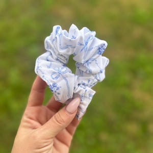 May include: A set of three ceramic mugs with a speckled, cream-colored glaze. Each mug features a different hand-painted floral design in shades of blue, green, and yellow. The mugs have a simple, rounded shape and a comfortable handle.