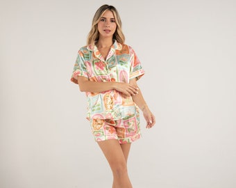 May include: A woman wearing a short-sleeved pajama top and matching shorts. The pajamas are made of satin and have a colorful floral print.