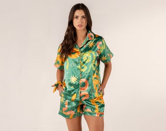 May include: A green satin pajama set with a short-sleeved button-up top and matching shorts. The fabric features a colorful print of snakes, stars, and other celestial symbols.