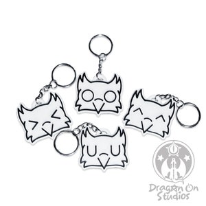 Może przedstawiać: Cztery białe breloki w kształcie sowy z różnymi wyrażeniami twarzy. Każdy brelok ma srebrny metalowy pierścień i łańcuszek. Breloki znajdują się na białym tle.