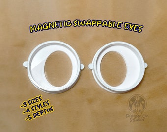 Pode incluir: Duas órbitas oculares de plástico branco com uma abertura redonda para olhos intercambiáveis magnéticos. O texto "MAGNETIC SWAPPABLE EYES" está no topo da imagem. O texto " -3 SIZES -4 STYLES -5 DEPTHS" está na parte inferior da imagem.