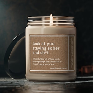 May include: A beige candle with a brown label that reads "look at you staying sober and sh*t"  infused with a bit of hard work, new beginnings and a whole lot of I'm so f*cking proud of you candle cozy corner.