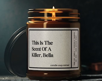 May include: A brown glass candle jar with a white label that reads "This Is The Scent Of A Killer, Bella" and "candle cozy corner". The candle is lit and the flame is visible.