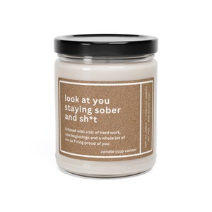 May include: A beige candle jar with a black lid. The label reads "look at you staying sober and sh*t" and "infused with a bit of hard work, new beginnings and a whole lot of I'm so f*cing proud of you." The label also says "candle cozy corner".