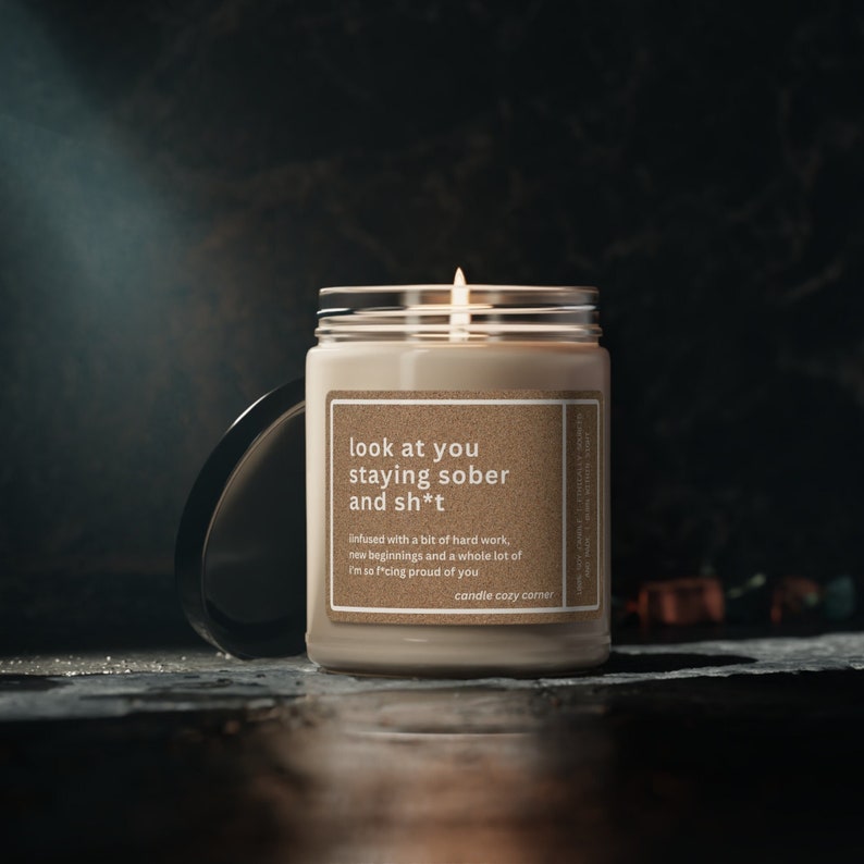 May include: A beige candle with a brown label that reads "look at you staying sober and sh*t"  infused with a bit of hard work, new beginnings and a whole lot of I'm so f*cking proud of you candle cozy corner.