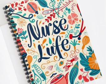 May include: Spiral-bound notebook with a cream-colored cover featuring the words "Nurse Life" in navy blue script. The cover is decorated with colorful illustrations of medical tools, flowers, and other decorative elements.