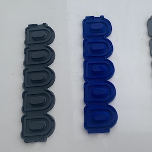 May include: Three flexible, rubbery strips in shades of gray and blue. Each strip has a series of raised, rounded rectangles. The strips are arranged vertically, with the colors being dark gray, blue, and light gray.