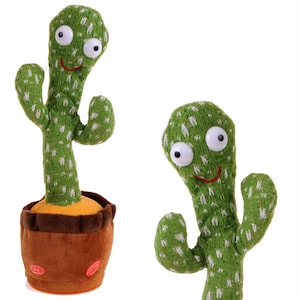 May include: A green cactus-shaped soft toy with large white eyes and a smiling red mouth. The toy is in a brown pot and has white speckles. The cactus has two arms and a long stem. The background is white.