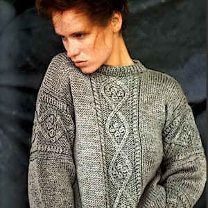 May include: A grey cable knit jumper with a detailed pattern. The jumper has a round neckline and long sleeves.