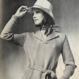 May include: A woman wearing a light brown sweater with a matching belt, a white hat, and a patterned scarf.