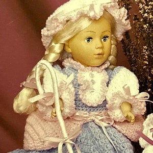 Puede incluir: Muñeca artesanal vestida de pastora, con un vestido y gorro de ganchillo azul y rosa. La muñeca sostiene un bastón blanco con cintas rosas y está acompañada de dos figuras de ovejas blancas con caras y patas negras.