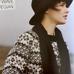 May include: A person wearing a black hat and a black and white patterned jumper with a black scarf. The jumper has a geometric design.