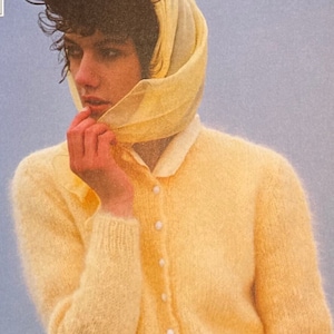 May include: A yellow cardigan with a button-up front and long sleeves. The cardigan is made of a soft, fuzzy material. The model is wearing a floral print skirt and a yellow scarf.