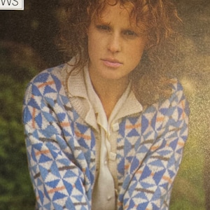 Può includere: Un cardigan bianco con un motivo geometrico blu, grigio e pesca. Il cardigan ha una chiusura con bottoni e maniche lunghe.