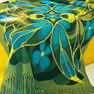May include: A green crocheted throw blanket with a blue and yellow floral pattern. The blanket has a fringe border.