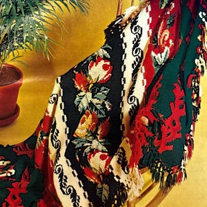 May include: A crocheted throw blanket with a floral pattern in shades of red, green, white, and black. The blanket is draped over a wooden rocking chair.