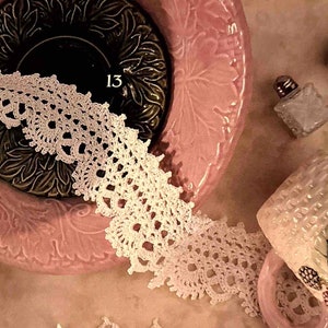 May include: A pink ceramic bowl with a floral design and a white crocheted lace trim. The bowl is sitting on a table with two small glass salt shakers and a white ceramic mug with a floral design.