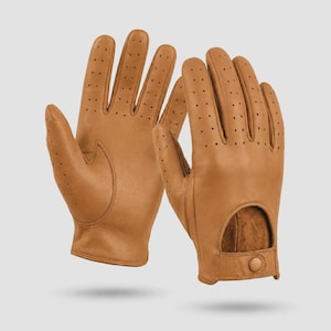 Puede incluir: Un par de guantes de conducir de cuero color canela con detalles perforados en los dedos y nudillos. Los guantes incluyen una abertura en el dorso de la mano y una pequeña correa con un cierre de botón a presión en la muñeca para ajustar.