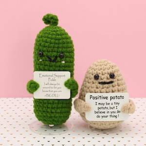May include: Two crocheted plushies, a green pickle and a brown potato, holding signs with encouraging messages. The pickle's sign reads "Emotional Support Pickle I will always be around to let you know that you are BIG DILL". The potato's sign reads "Positive potato I may be a tiny potato, but I believe in you. Go do your thing!"