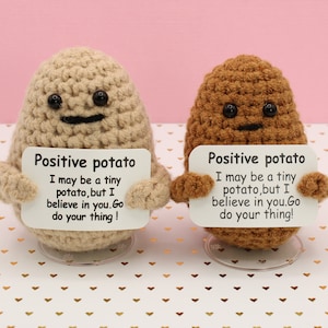 May include: Two crocheted potato plushies holding signs that say "Positive potato I may be a tiny potato, but I believe in you. Go do your thing!" The plushies are on a white background with gold hearts.