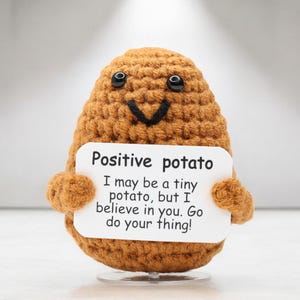 May include: A crocheted potato toy holding a sign that reads "Positive potato I may be a tiny potato, but I believe in you. Go do your thing!"
