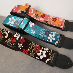 May include: Three guitar straps with floral patterns. One strap is pink with yellow and red flowers, another is teal with white and purple flowers, and the third is brown with red and white flowers. All have black leather ends.