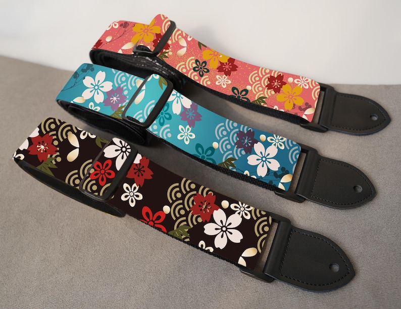 May include: Three guitar straps with floral patterns. One strap is pink with yellow and red flowers, another is teal with white and purple flowers, and the third is brown with red and white flowers. All have black leather ends.