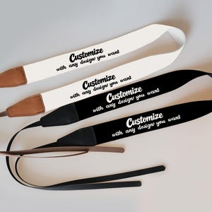 May include: Three camera straps in white, black, and brown. Each strap has the text "Customize with any design you want" in black. The straps have leather and black fabric accents.