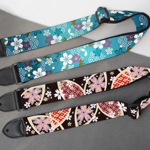 May include: Three guitar straps with floral patterns. One strap is teal with white and purple flowers and a wave design. The other two straps are brown with pink and white flowers and geometric shapes. All straps have black leather ends.