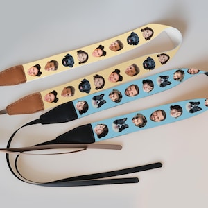 May include: Three camera straps with custom face prints. One strap is yellow, another is light blue, and the third is black. Each strap has a brown leather end piece and a black strap. The straps are decorated with various faces.