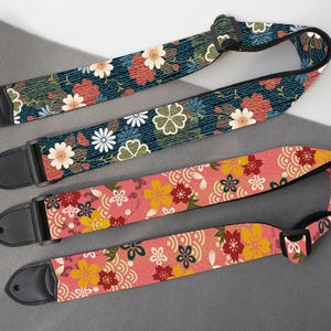 May include: Three guitar straps with floral patterns. One strap has a navy blue background with red and white flowers. Another has a pink background with yellow and red flowers. The third strap has a green background with red and white flowers. Each strap has black leather ends.