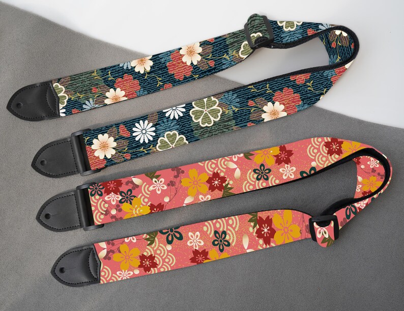 May include: Three guitar straps with floral patterns. One strap has a navy blue background with red and white flowers. Another has a pink background with yellow and red flowers. The third strap has a green background with red and white flowers. Each strap has black leather ends.
