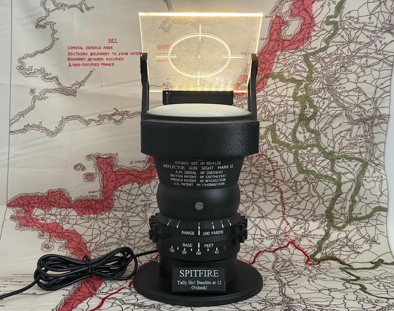 May include: A black reflector gun sight, Mark II, with a clear, illuminated screen and a circular target reticle. The base reads "SPITFIRE" and "Tally Ho! Bandits at 12 O'clock!". The sight is set against a map background with a coastal defense area key.