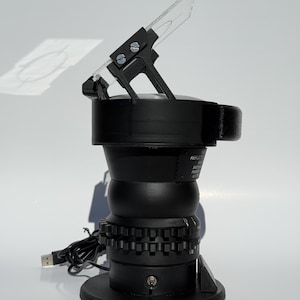 May include: Black optical instrument with a clear, angled lens. The device has a cylindrical body with a series of gears and a USB cable. The instrument is designed to reflect light, as indicated by the text on the side.
