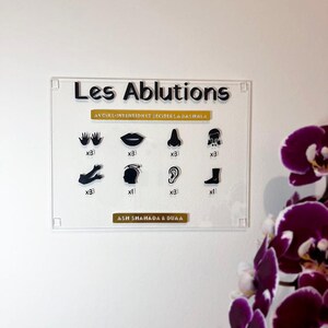 Peut inclure: Panneau acrylique transparent avec le texte "Les Ablutions" et des illustrations de parties du corps. Le panneau comprend le texte "AVOIR L'INTENTION ET RECITER LA BASHALA" et "ASH SHAHADA & DUAA". Une orchidée violette est en arrière-plan.