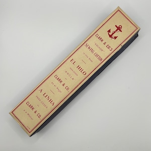 May include: A vintage box of Clark & Co's "Anchor" sewing cotton. The box is cream coloured with red text and an anchor logo. The text reads "Clark & Co's "Anchor" Sewing Cotton is the Best."  "El Hilo Para Coser "Ancla" Clark & Co. es el Mejor."  "A Linha Para Coser Clark & Co. é a Melhor."