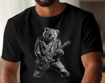 Puede incluir: Una camiseta negra con un gráfico de un oso tocando una guitarra eléctrica. El oso lleva una chaqueta de cuero y pantalones vaqueros. El gráfico está en tonos grises.