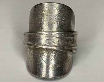 Pode incluir: Um anel de prata feito de uma colher reutilizada. O anel é largo e tem um design único e texturizado.