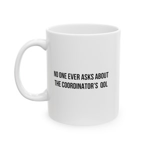 May include: White ceramic mug with a curved handle. The mug features black text that reads, "NO ONE EVER ASKS ABOUT THE COORDINATOR'S QOL."