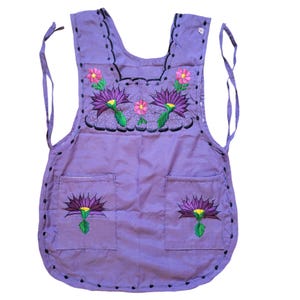 May include: A purple apron with embroidered flowers in shades of purple, pink, green, and yellow. The apron has two pockets and adjustable straps.