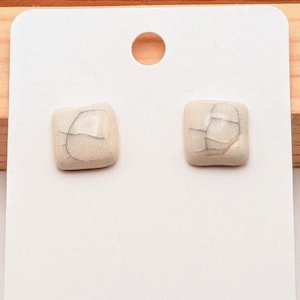 May include: A pair of white ceramic square earrings with a crackled glaze finish.