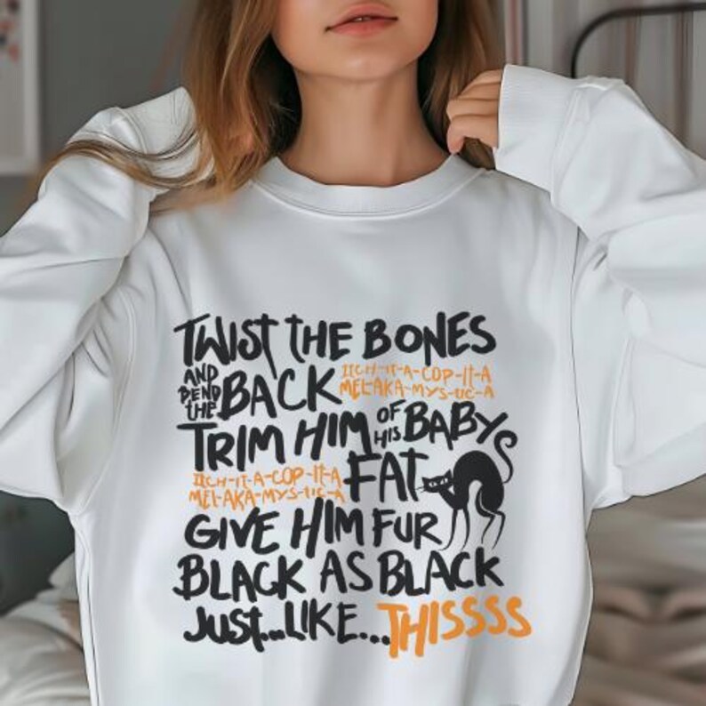 K&ouml;nnte beinhalten: Wei&szlig;er Pullover mit einem schwarzen und orangefarbenen Grafikdruck, auf dem "Twist the bones and bend the back, trim him of his baby's fat, give him fur black as black just...like...thissss" steht.